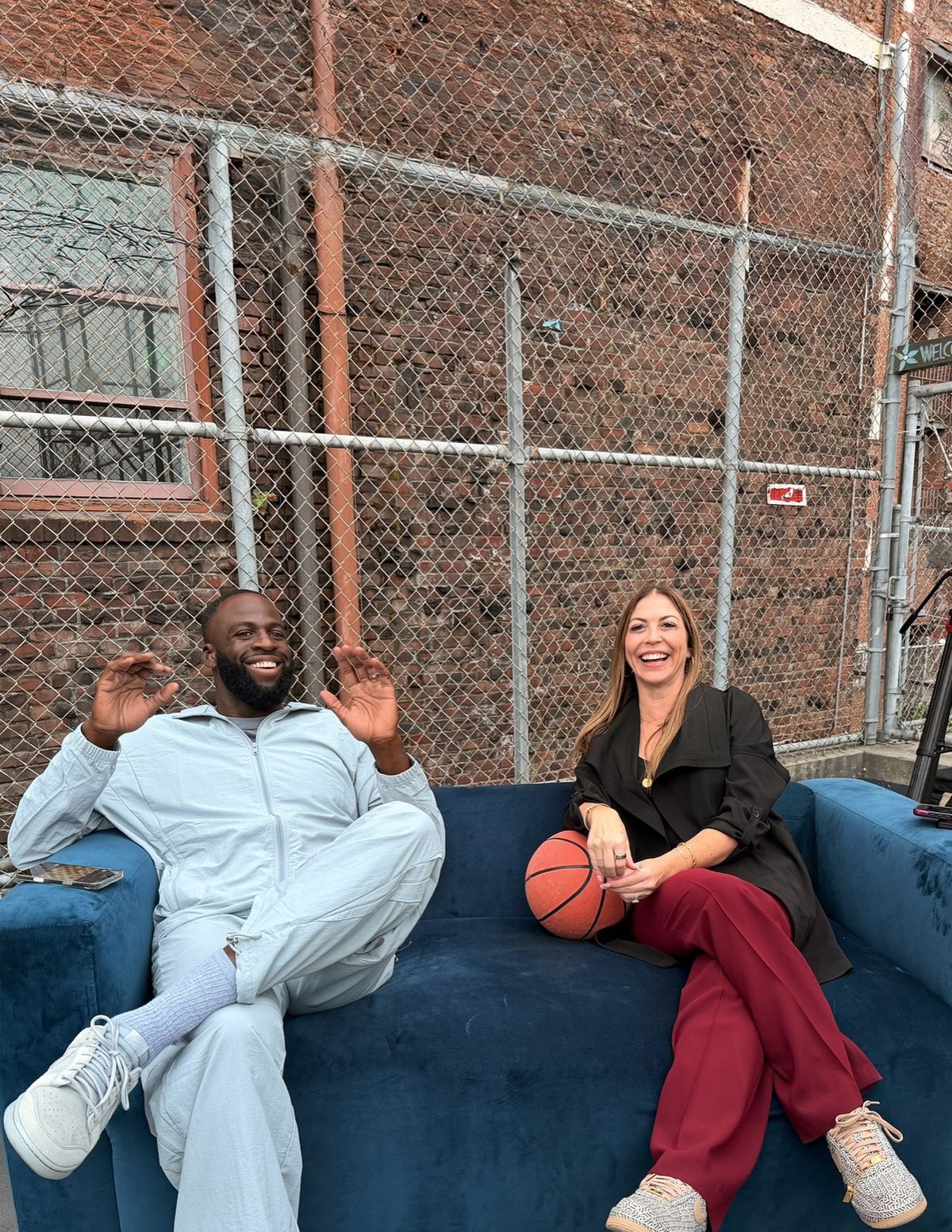 Draymond Green and Dana Hooper on a blue sofa on an outdoor court during a shoot
