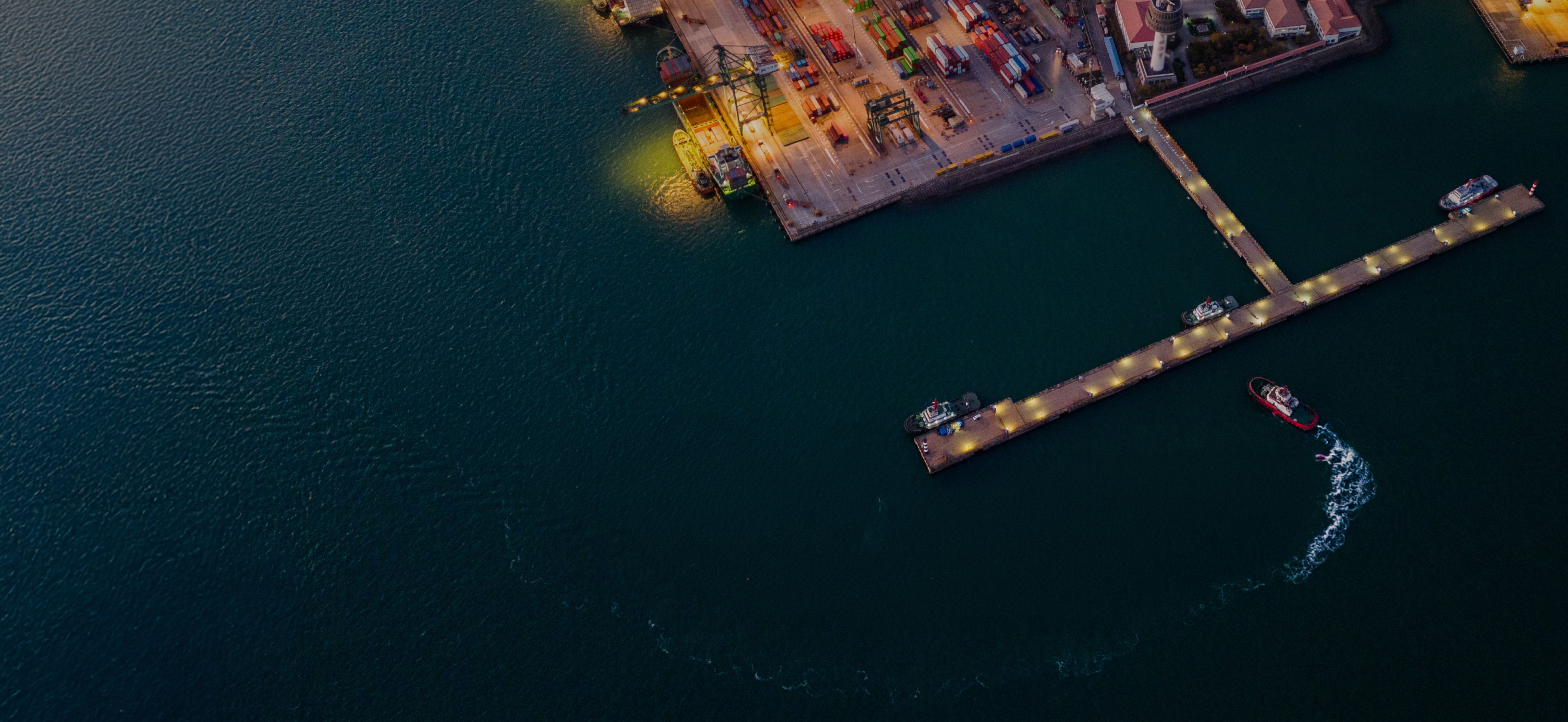 Aerial view of boats on water near a dock, with lights illuminating the pier and surrounding area.