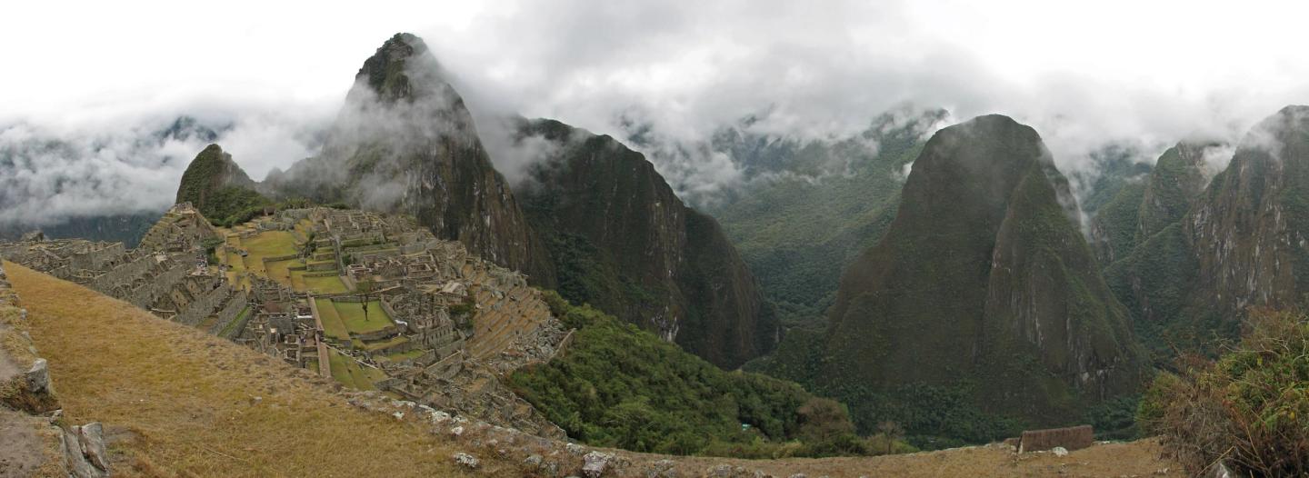 Los edificios de piedra y las terrazas de Machu Picchu, rodeados de montañas verdes entre las nubes.