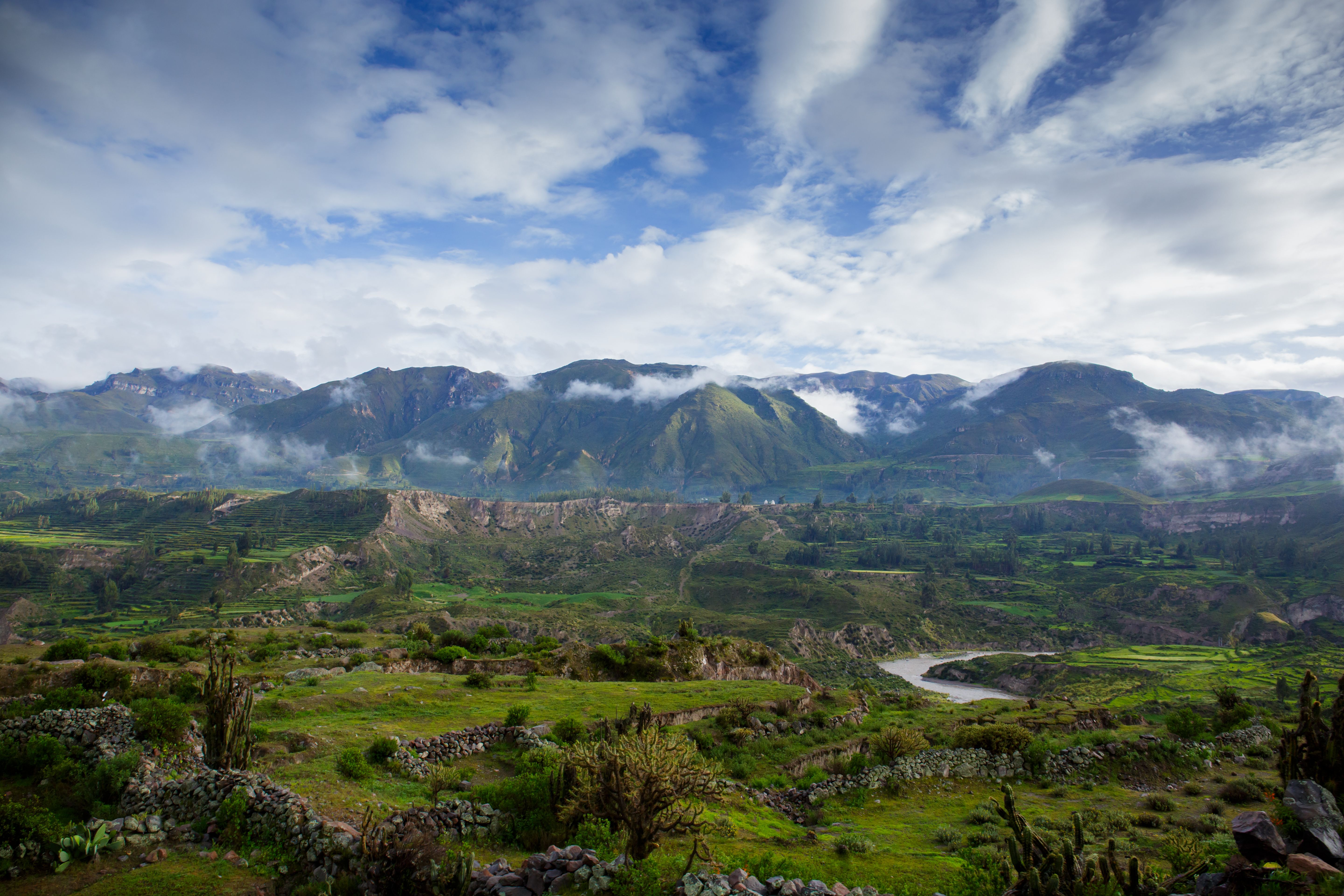Green terraces and the river in the Colca Valley beneath a cloudy sky.