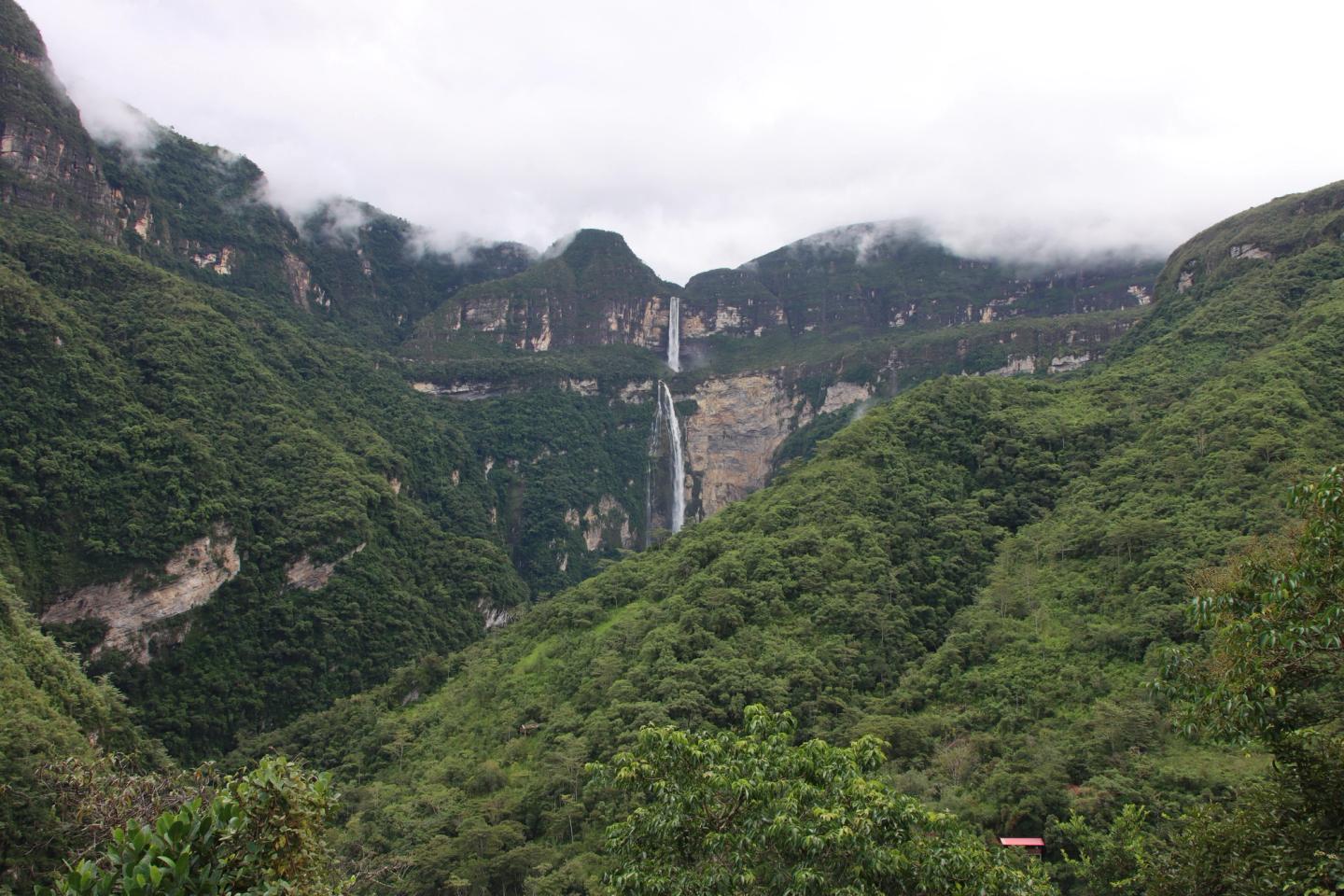 The two drops of Gocta waterfall between green mountain slopes and low clouds.