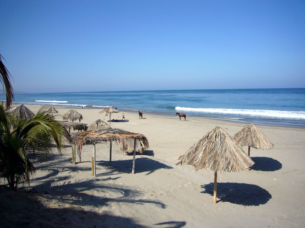 Palm-thatch parasols on Máncora's sandy beach, with the blue sea beyond.