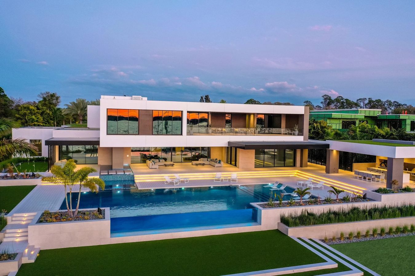 Modern luxury estate photographed at twilight with illuminated interior and a deep blue Florida sky