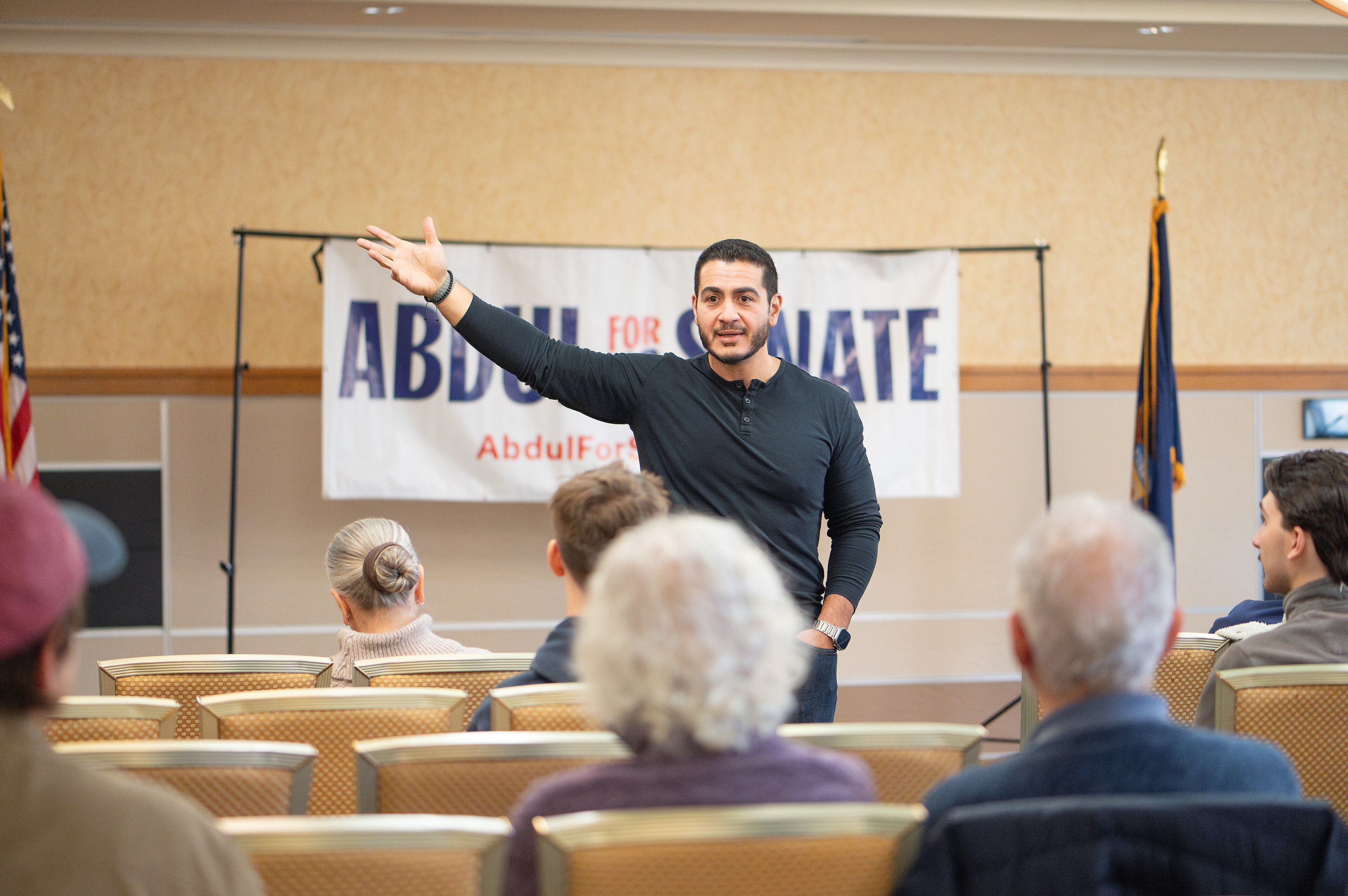 Abdul El-Sayed speaking at a campaign meet-and-greet in front of an "Abdul for US Senate" banner