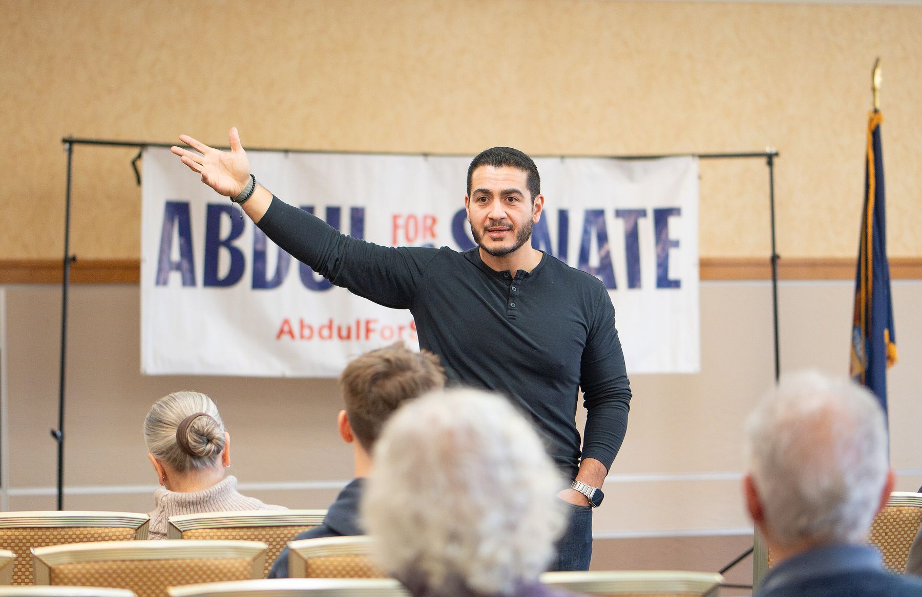 Abdul El-Sayed speaking at a campaign meet-and-greet in front of an "Abdul for US Senate" banner