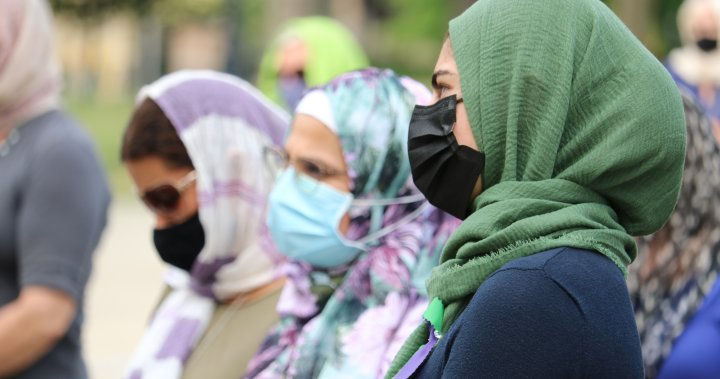A woman wearing a white hijab, a mask on her face, while standing.