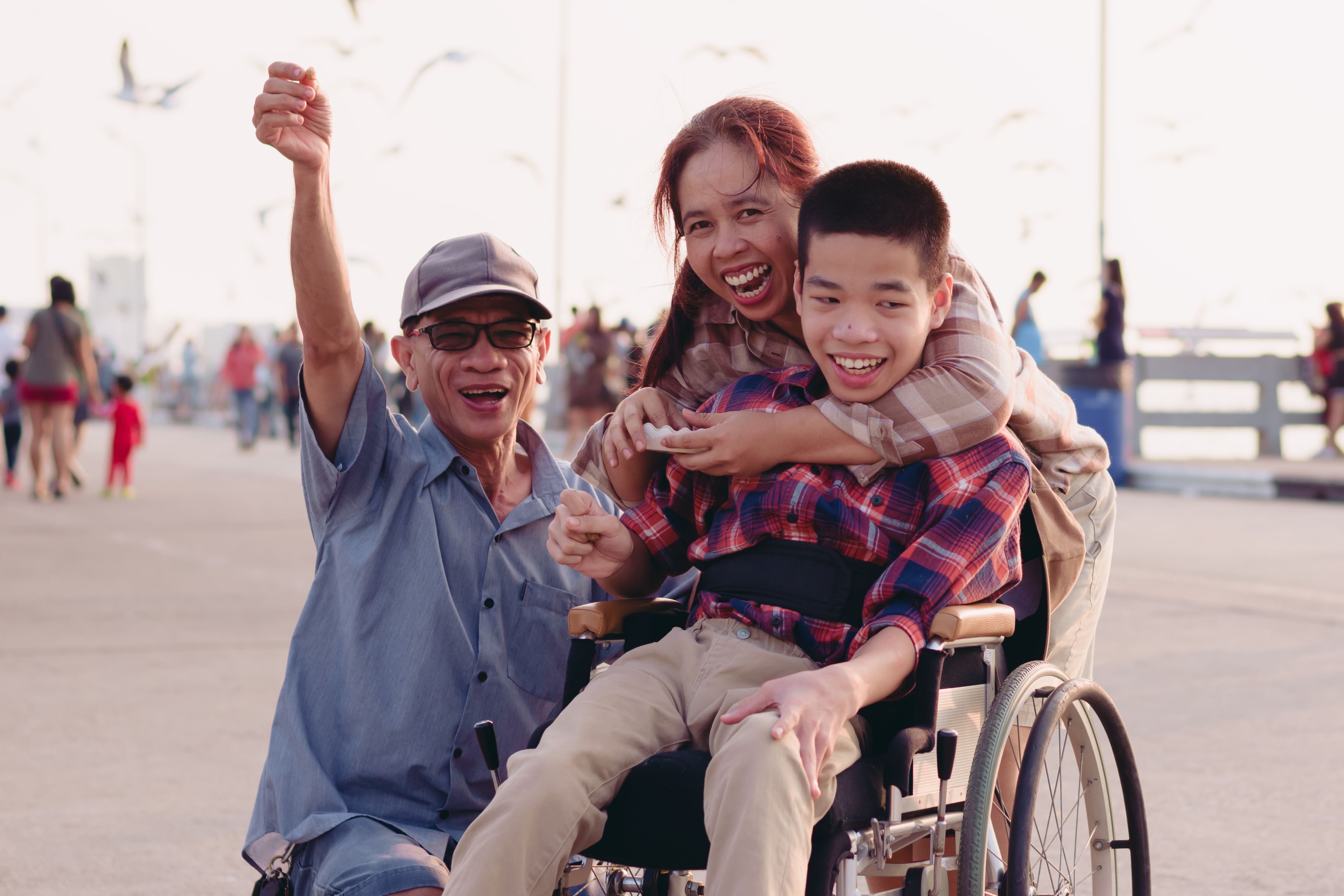 a young boy in a wheelchair being hugged by his smiling Mum beside his Dad