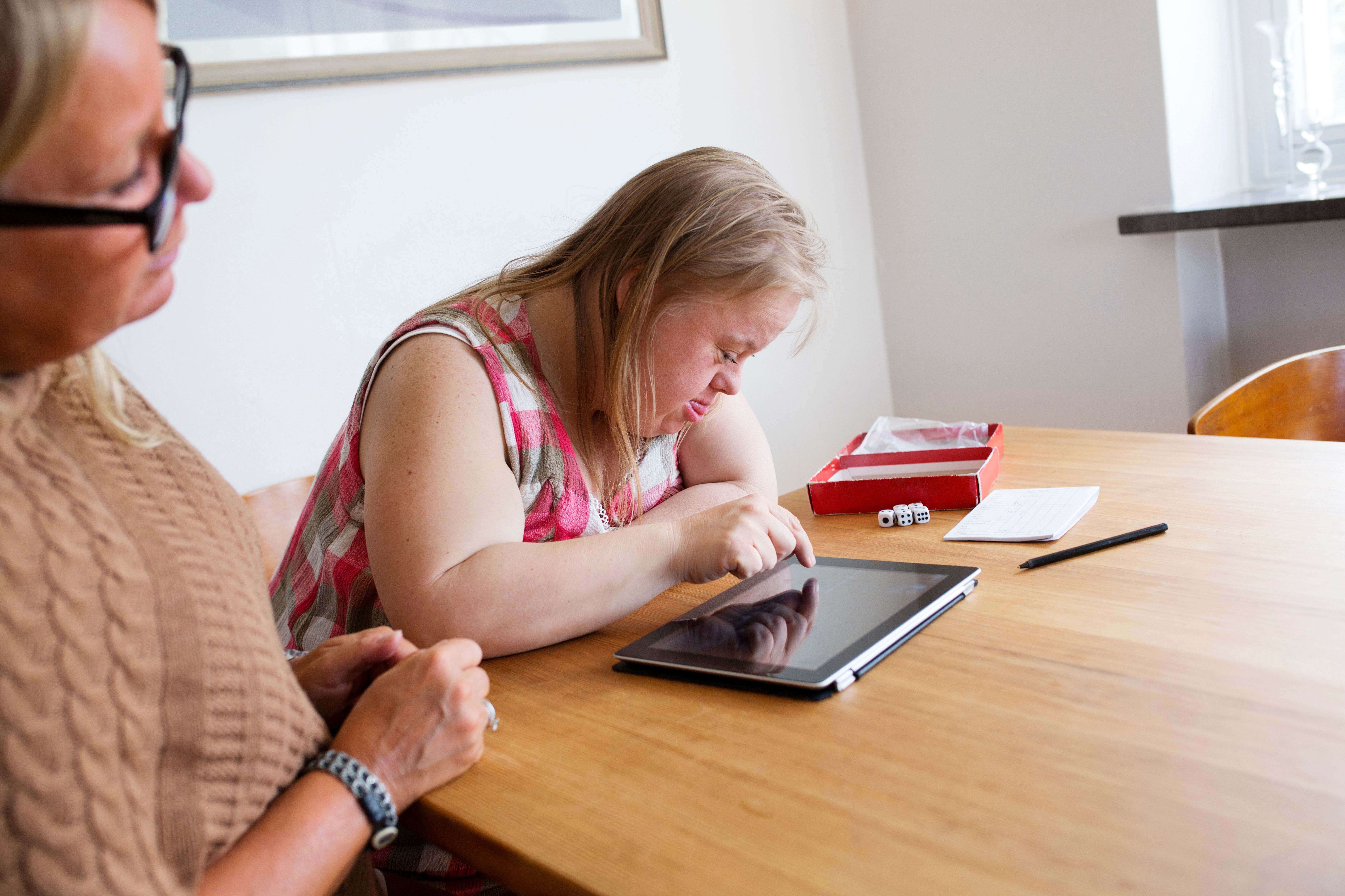 a woman with downe syndrome operating a tablet device while sitting at a table with a Speech Pathologist 