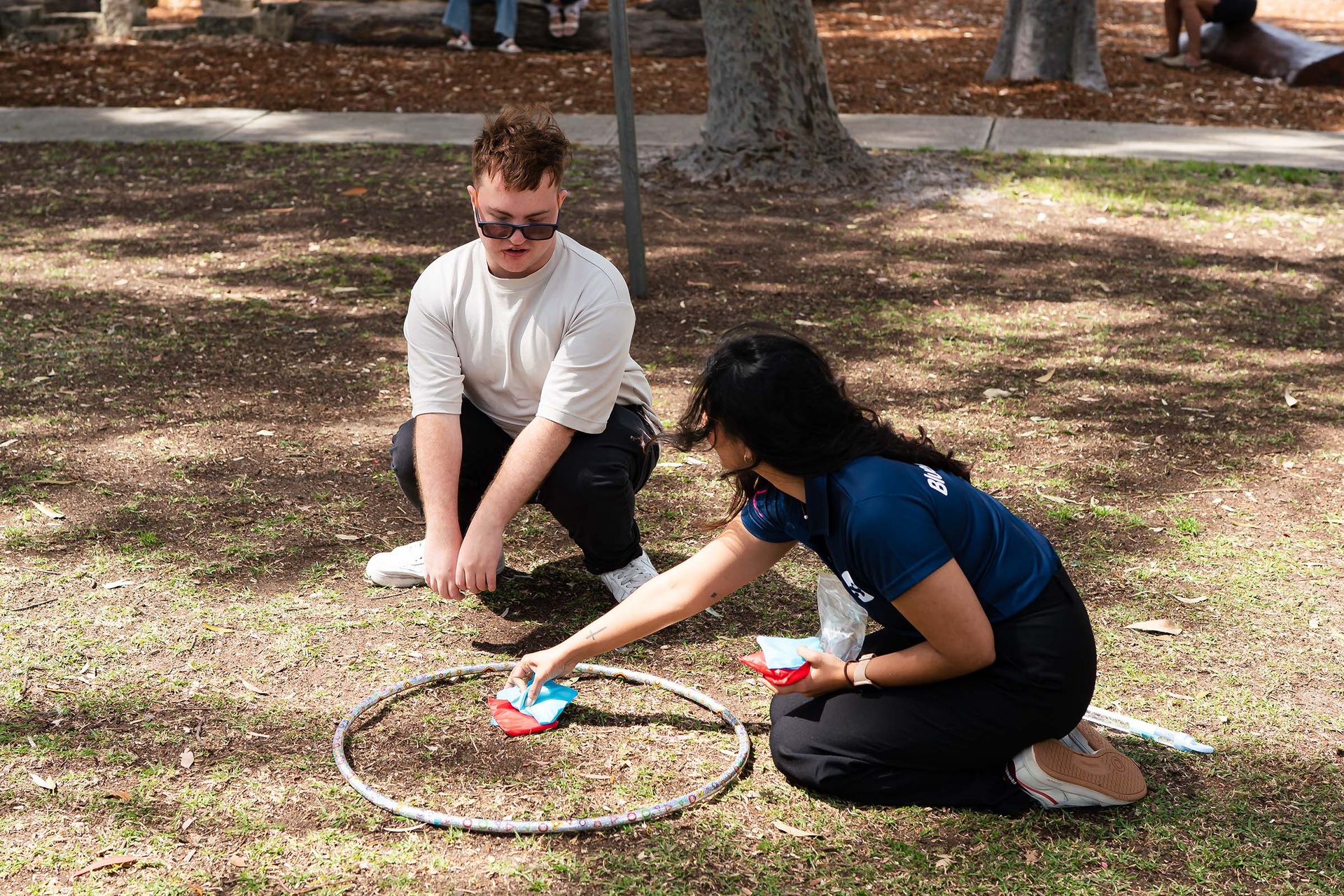 A boy crouching down beside a hula hoop next to a BlueRocket clinician who is holding mini bean bags