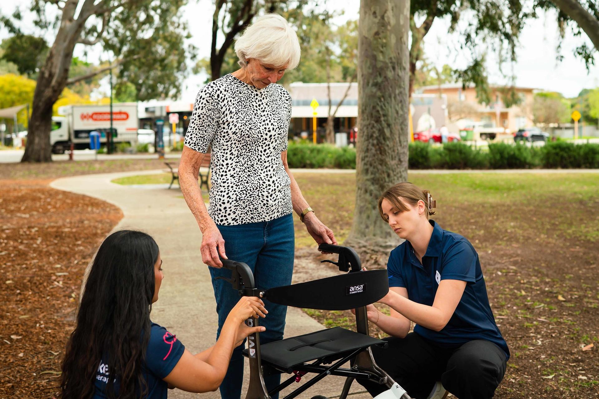 Elderly woman standing with walking frame, with two BlueRocket clinicians adjusting it for her