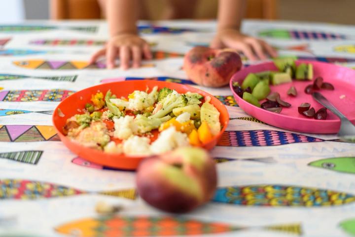 a plate of half-eaten vegetables on a table with a child's hands resting on table behind