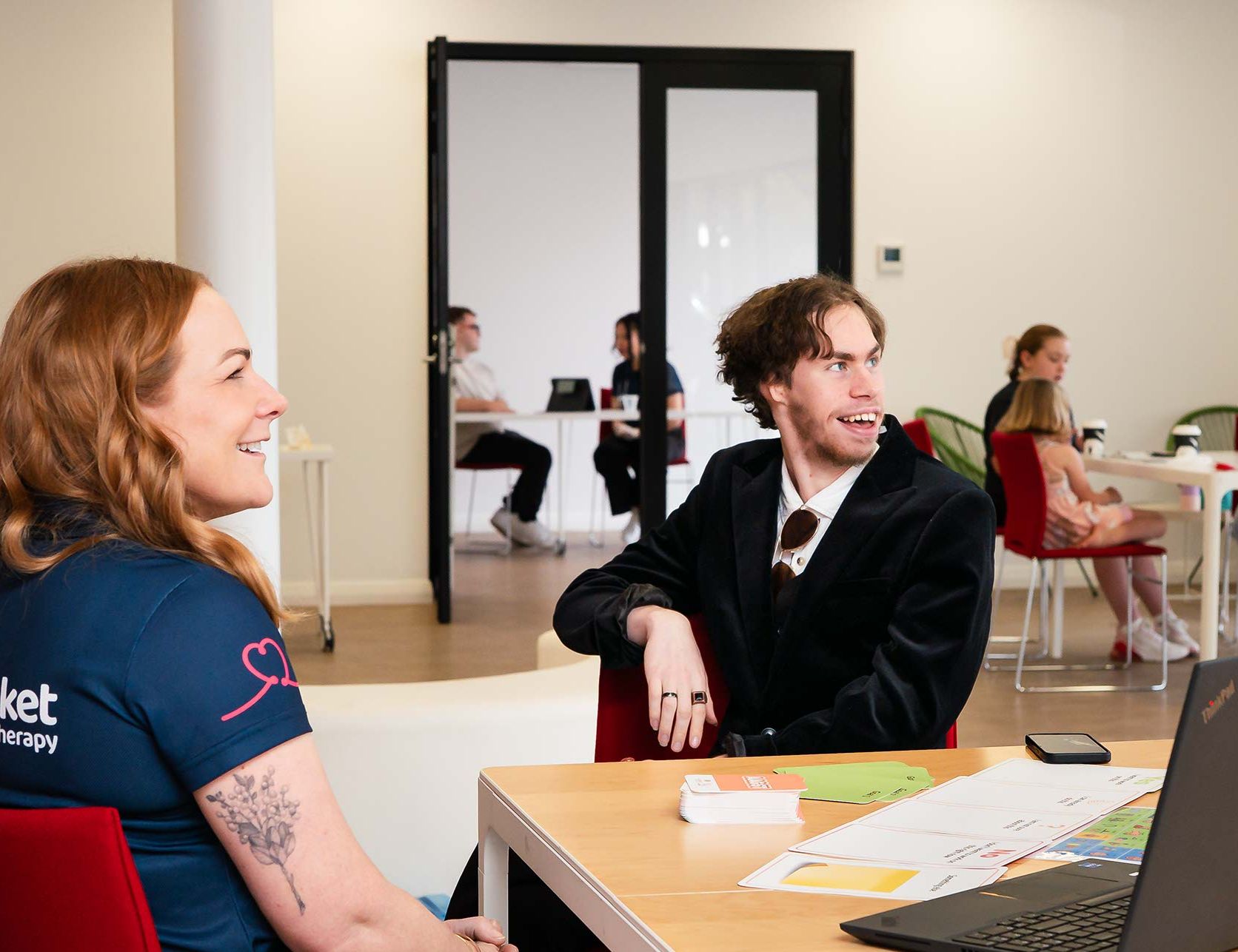 A BlueRocket clinician sitting with a man with cards on a table and a laptop.