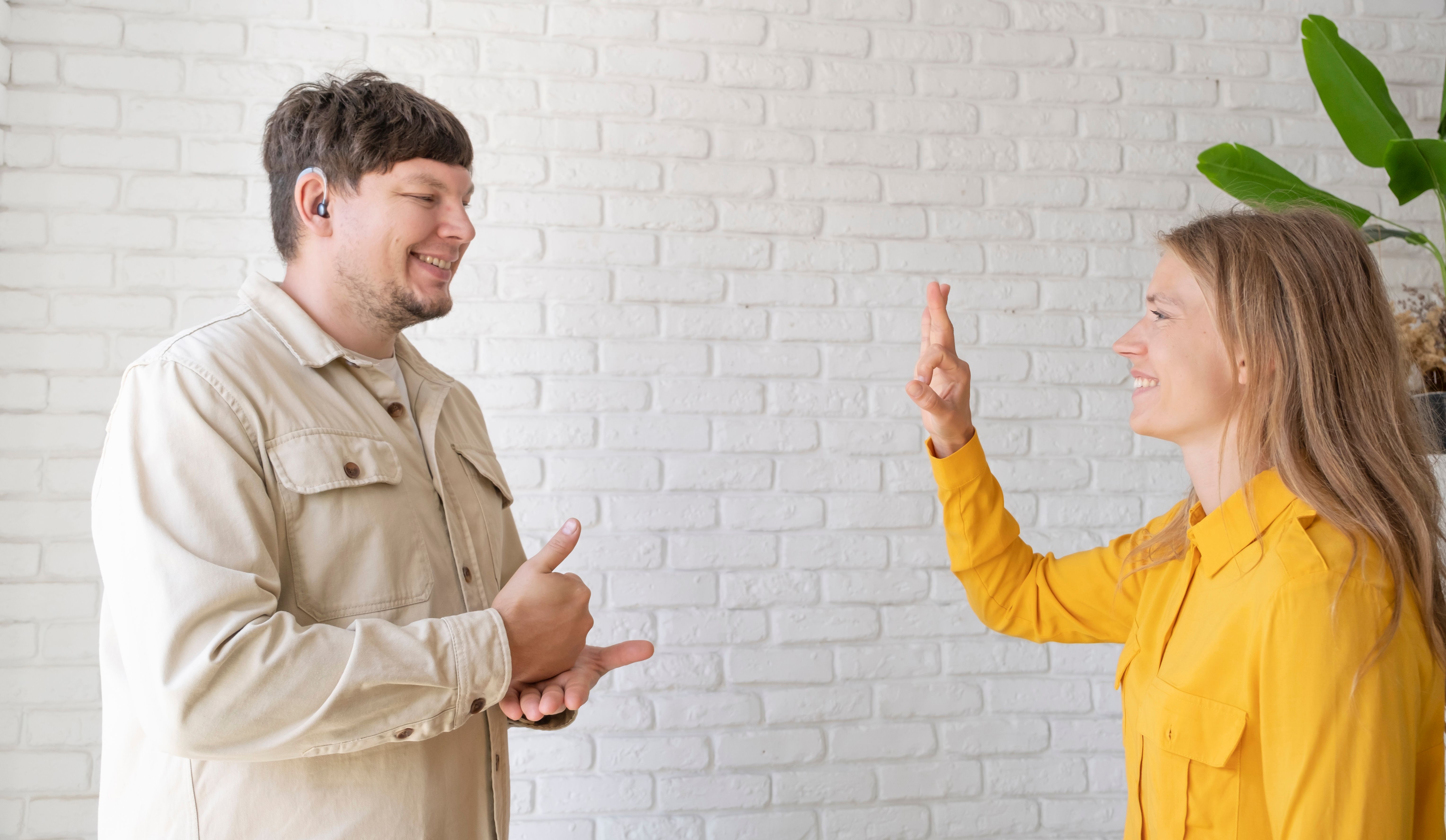 a smiling man wearing a hearing aid communicating with a female Speech Pathologist via sign language