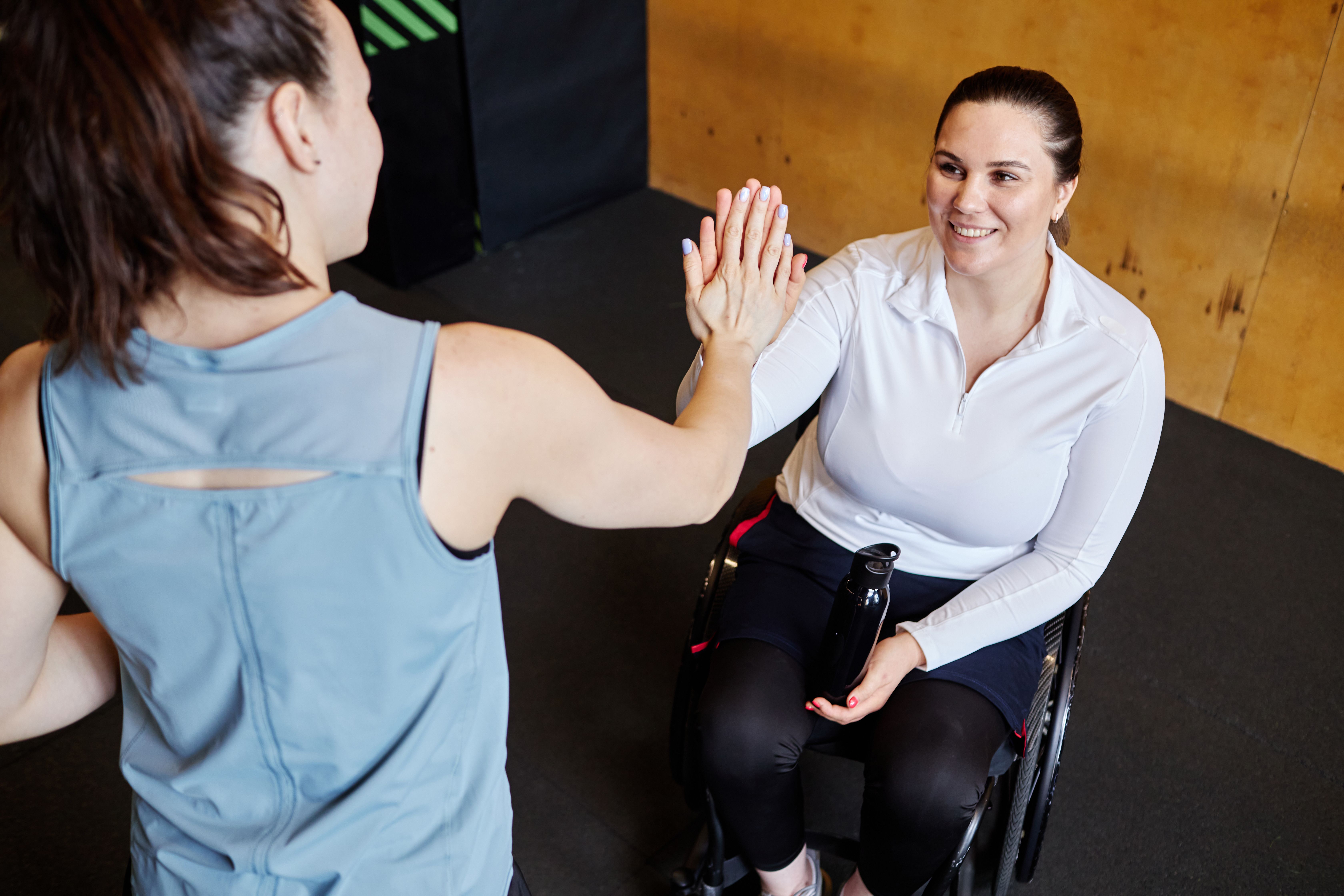 smiling woman in wheelchair high fiving fitness instructor standing in front of her