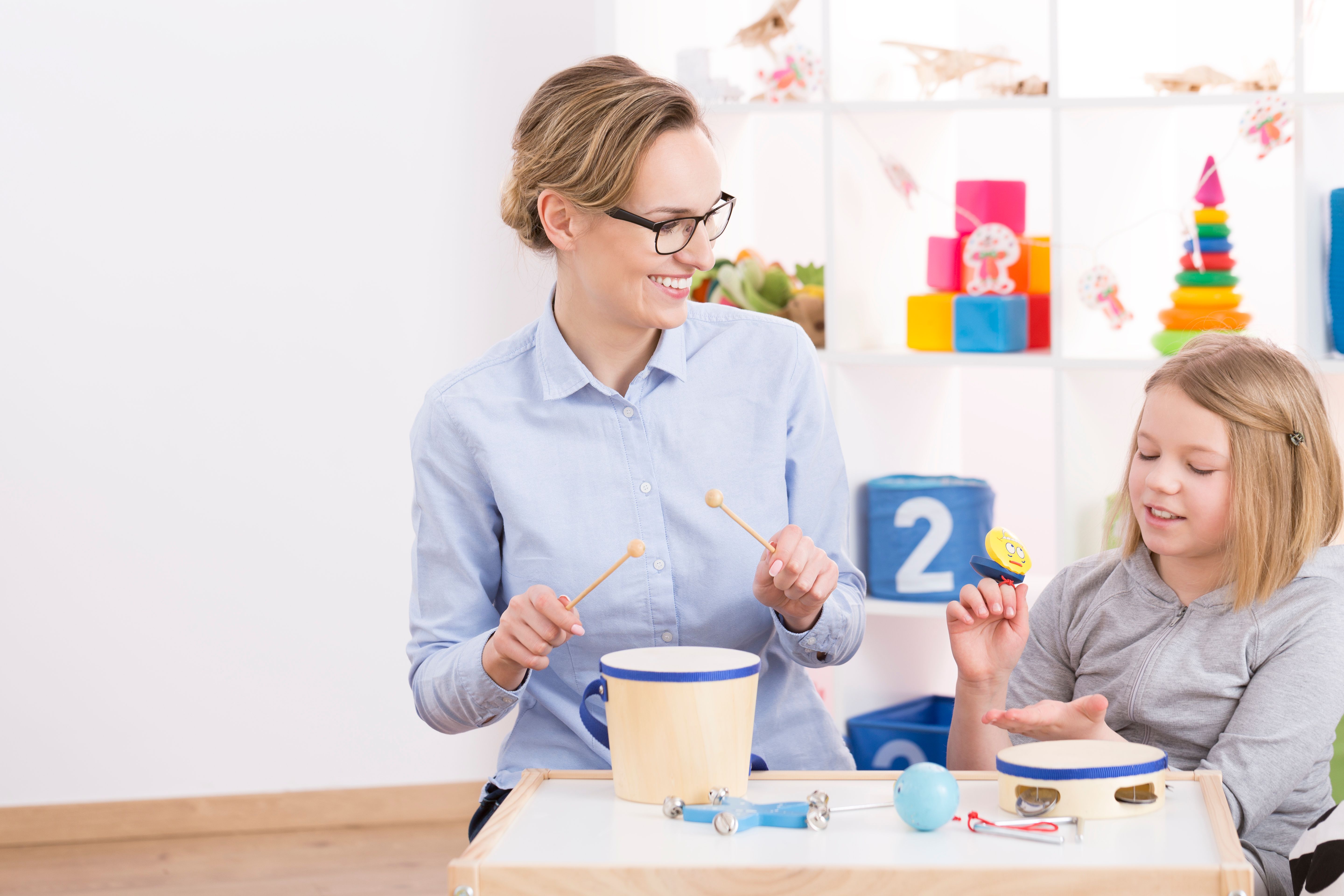 Woman and young girl sitting at a table playing with toy musical instruments, both smiling