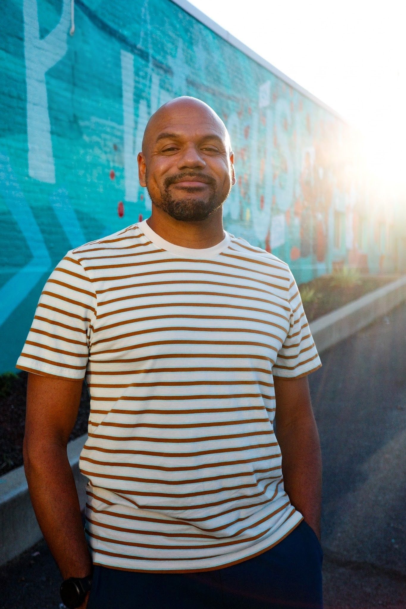 Ken Jones outdoors in a striped shirt, in front of a teal mural