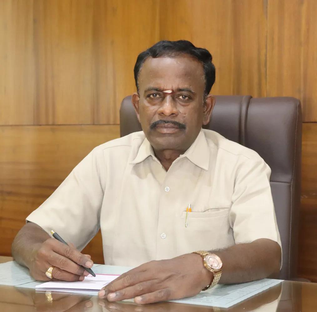 SMBM Matric Correspondent seated at desk, posing formally with documents.