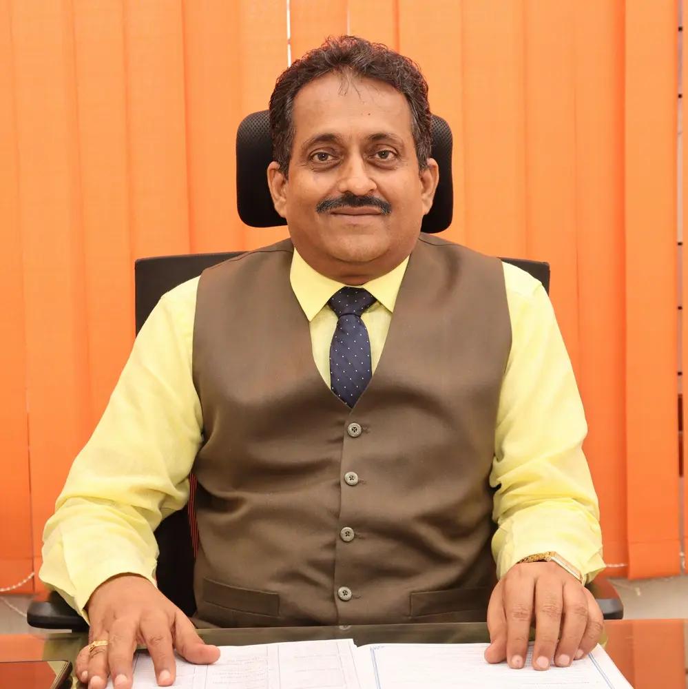 SMBM Matric Principal seated at desk, posing formally in office setting.