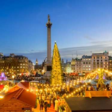 Blick auf den Trafalgra Square an Weihnachten in London. Im Hintergrund der berühmte Weihnachtsbaum, der gegen die Abenddämmerung beleuchtet wird.