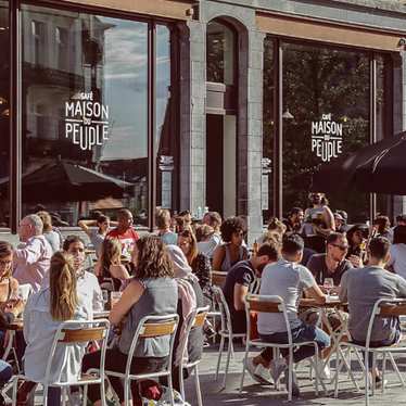 People sitting outside Café Maison du Peuple on a sunny day.