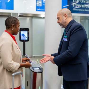 A traveler shows her ticket to a staff member at an automated gate in a train station.
