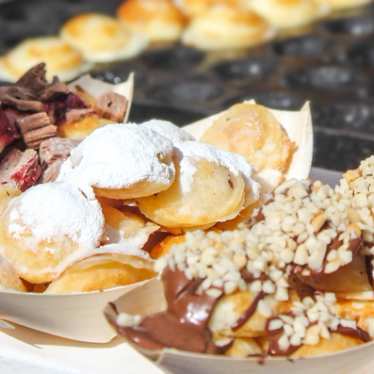 A pile of poffertjes covered in powdered sugar and chocolate.