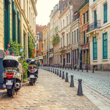 Two mopeds parked on a cobbled pavement on a street of traditional terraced buildings in Lille.
