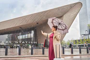 Rotterdam Centraal: Frau mit Regenschirm hält Hand nach Taxi aus