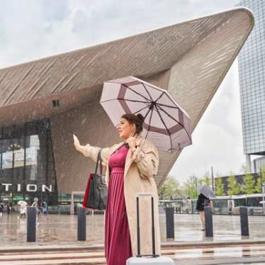 Rotterdam Centraal: Frau mit Regenschirm hält Hand nach Taxi aus