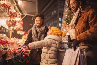 Een gelukkig gezin, een jongen, een vrouw en een man, stopt bij een kraam op een Parijse kerstmarkt. Het kleine kind wijst naar wat Lebkuchen kerstkoekjes terwijl de moeder en vader glimlachen. 