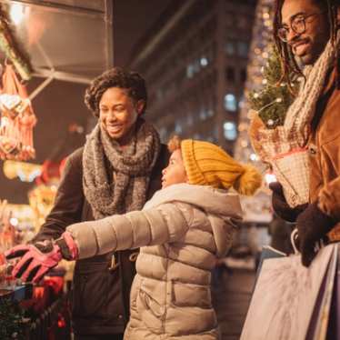 Een gelukkig gezin, een jongen, een vrouw en een man, stopt bij een kraam op een Parijse kerstmarkt. Het kleine kind wijst naar wat Lebkuchen kerstkoekjes terwijl de moeder en vader glimlachen.