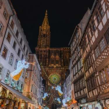 Nachtbeeld van een Belgische straat die naar de kathedraal leidt, verlicht met feestelijk verlichte engelen en trompetten.