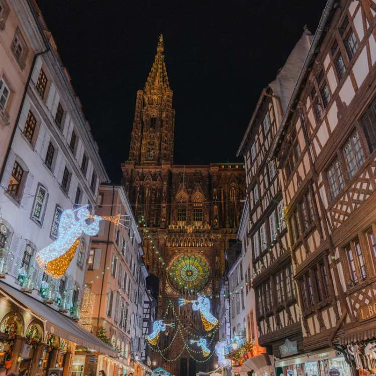 Nighttime image of a Belgian street leading up to the cathedral, illuminated with festive lit angels and trumpets.