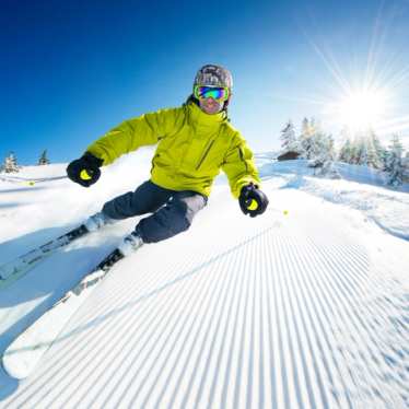 Smiling man wearing a lime green jacket skiing down a slope