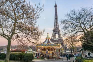 Paris im Winter: Ein Blick auf den Eiffelturm mit einem alten, erleuchteten Karussell davor.