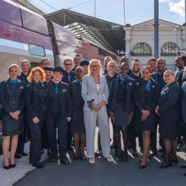 A large group of uniformed train staff stand together outside a train, smiling for a group photo.