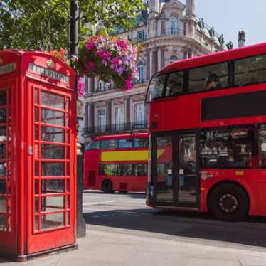 Street-level view of London red busses on a sunny day.