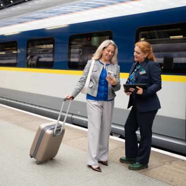 Une agente de train échange avec une passagère qui consulte son téléphone sur le quai, à côté du train