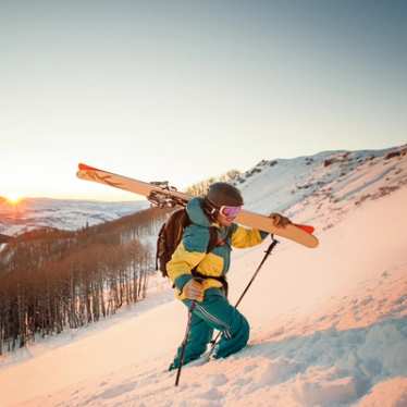 Guy with skis hiking during sunset