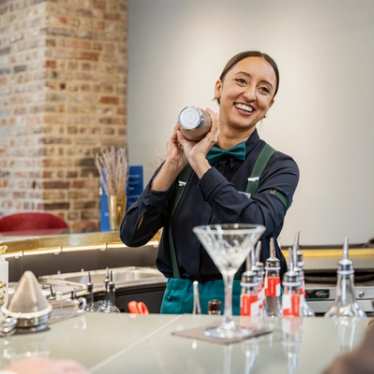 A bartender smiles while preparing a drink behind the bar.