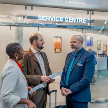 Un membre du personnel discute avec deux passagers tenant leurs documents de voyage devant un centre de service.