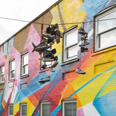 Shoes tied together by their laces that have been thrown over a telephone wire in front of some street art.