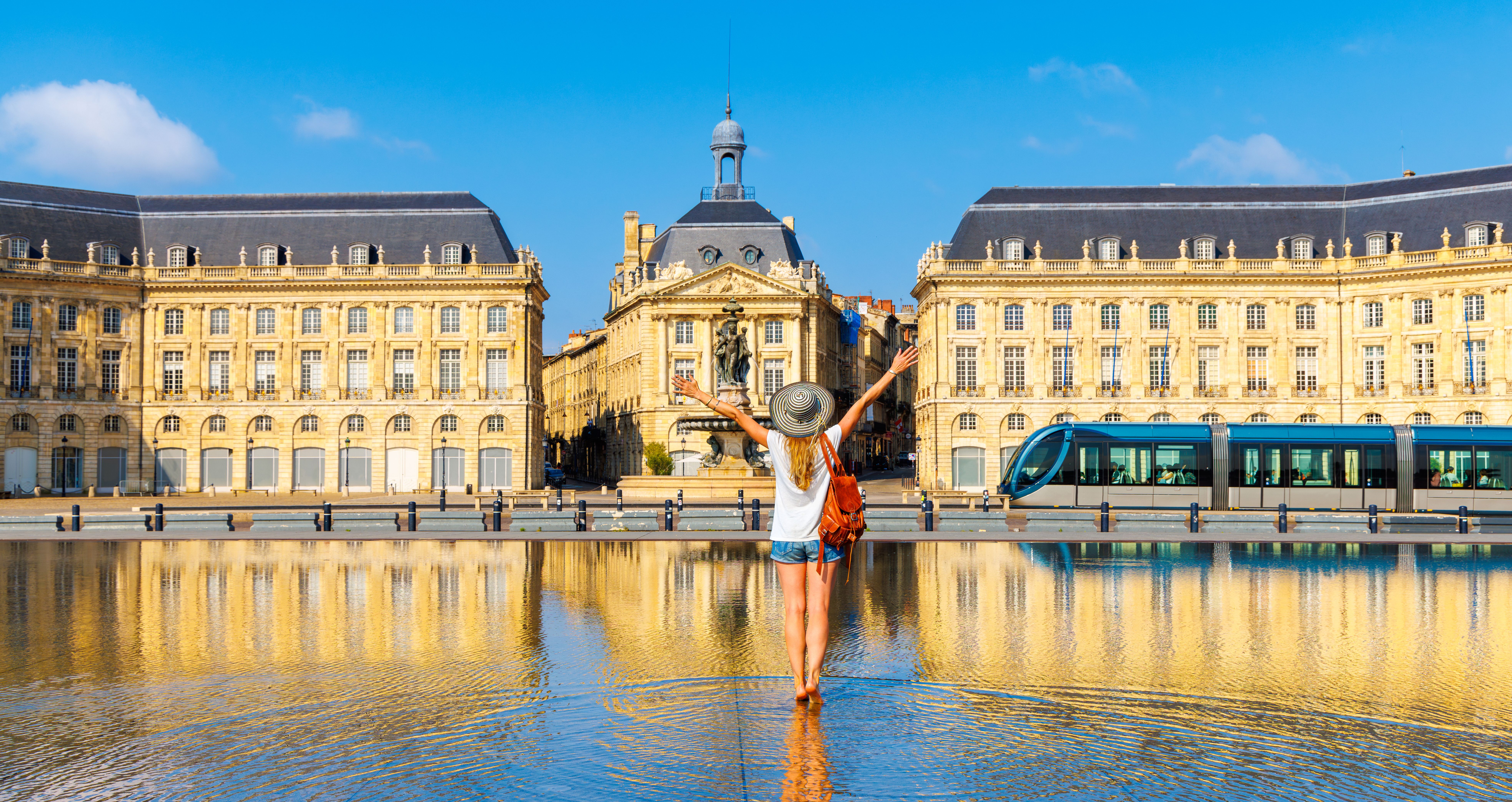 Touriste heureuse, les bras levés, sur la place de la Bourse avec miroir d'eau, paysage urbain de Bordeaux.