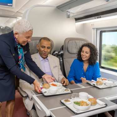 A staff member serves meals to two passengers seated together on the train.
