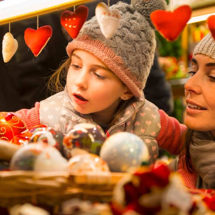 Close-up of a mother and daughter selecting decorations at the beautiful Les Halles Paris Christmas market. Their joyful expressions capture the festive spirit. Best reached by Eurostar for a heartwarming holiday experience.