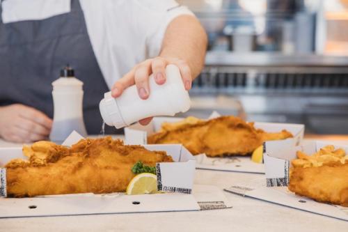 Man putting salt on fish and chips.