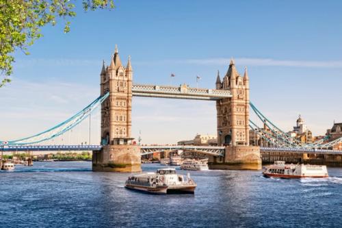 Thames river cruises passing under Tower Bridge on a sunny summer day.