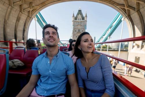A man and a woman on a tourbus as it goes over Tower Bridge.