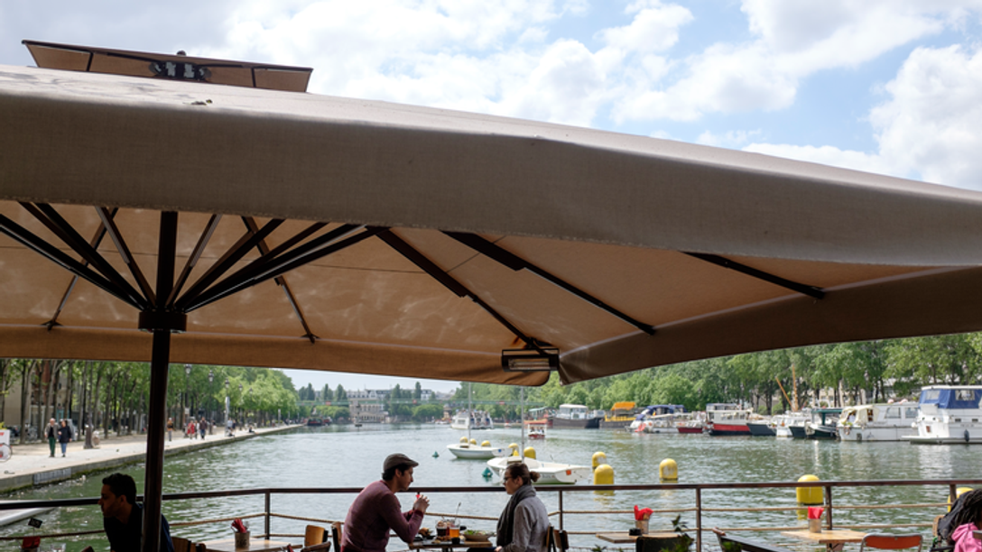 People eating at a restaurant by the Seine on a sunny day.