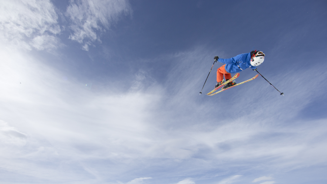 A man, mid-air, skiing in the Alps on a sunny day.